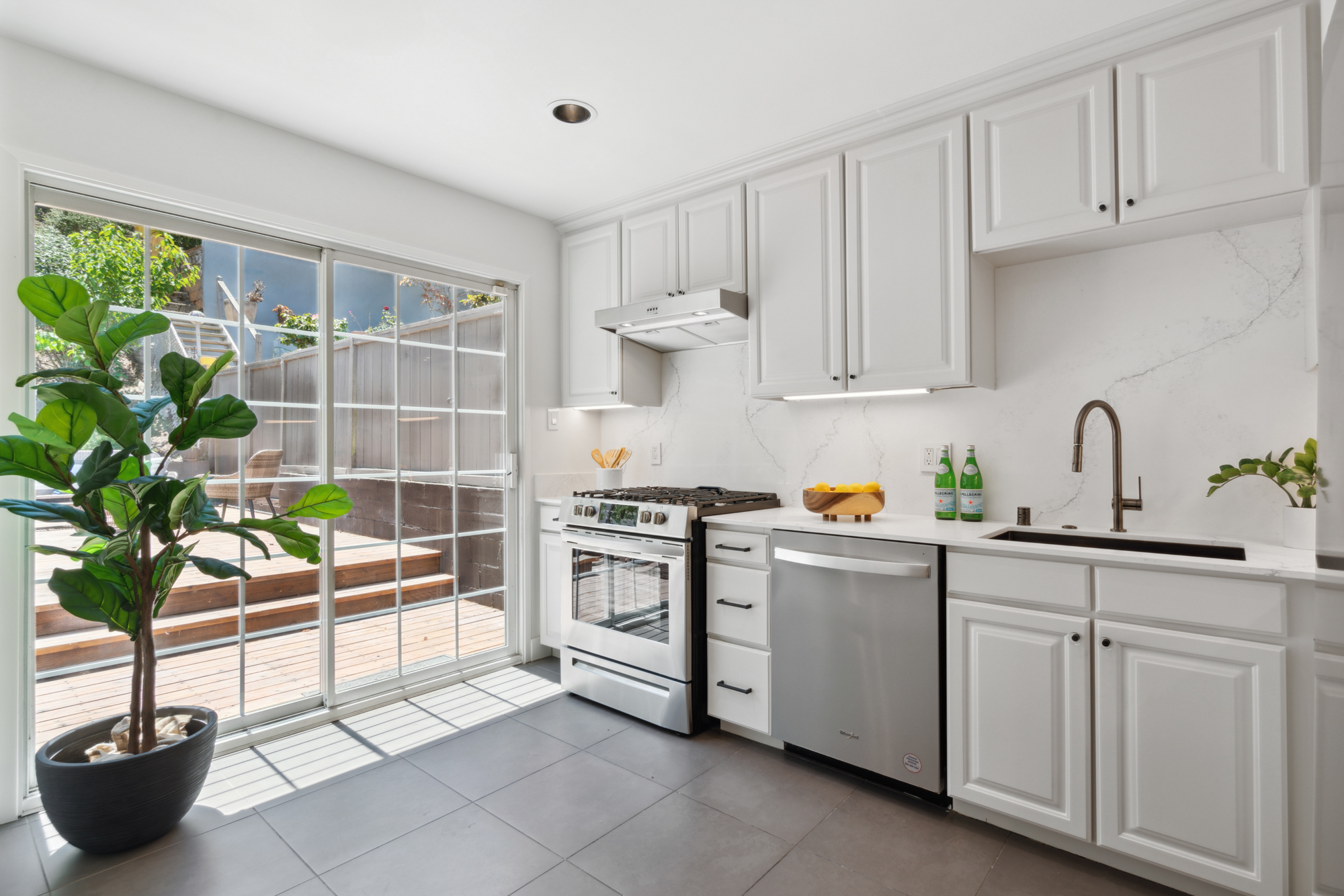 A lightly colored and updated kitchen with new quartz counters and backsplash and stainless appliances with sliding door to backyard