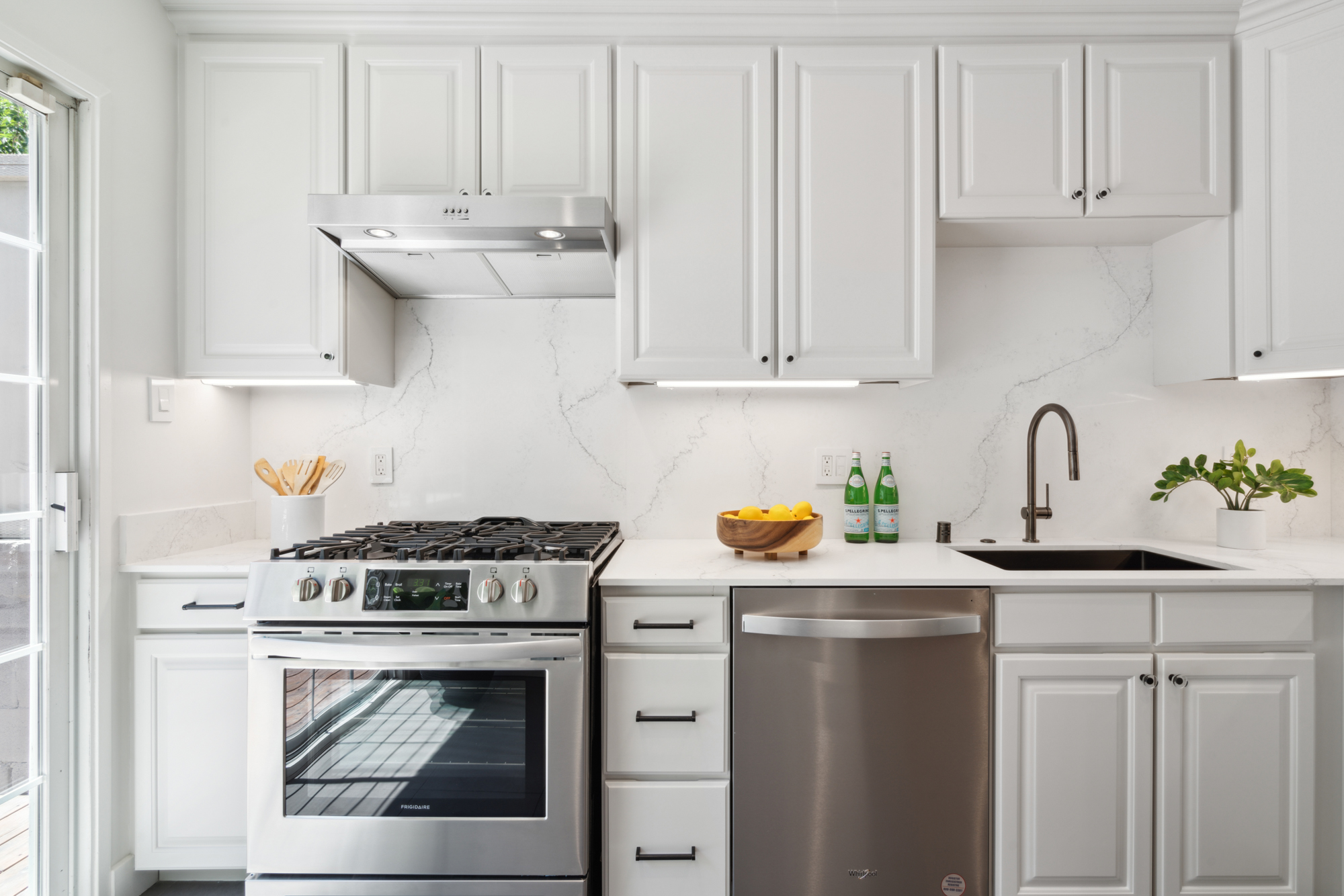 A lightly colored and updated kitchen with new quartz counters and backsplash and stainless appliances