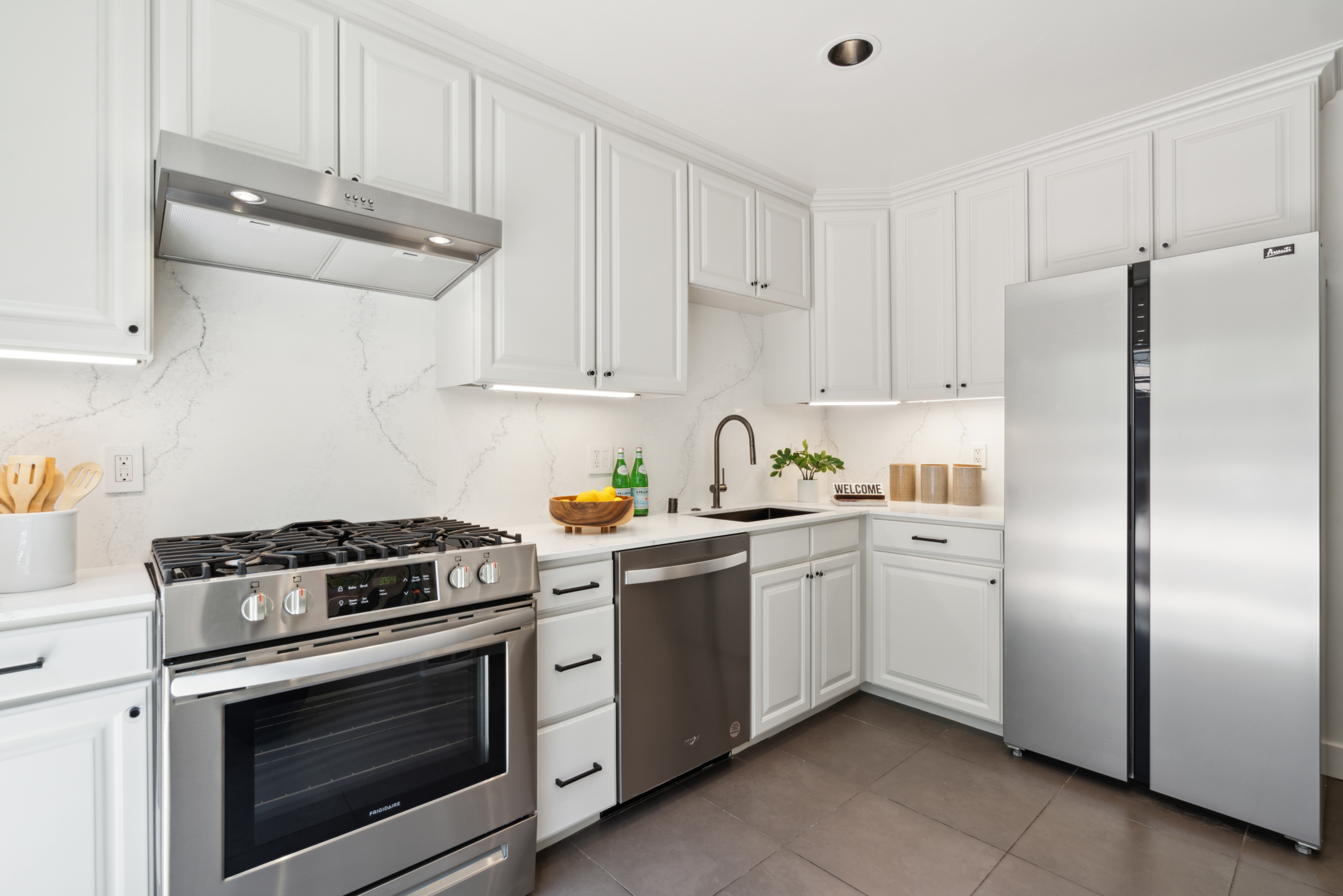 A lightly colored and updated kitchen with new quartz counters and backsplash and stainless appliances