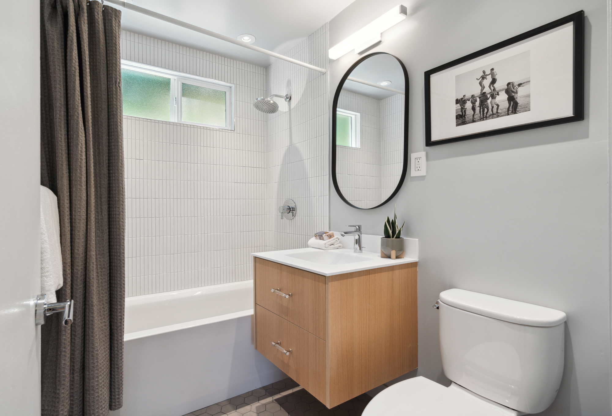 A three-piece bathroom with white tile, tub, floating oak vanity and hex tile floors in gray
