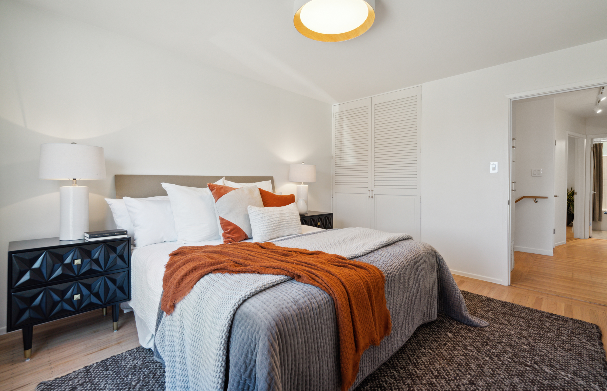 The front bedroom with a king-sized bed and LED light overhead, wood floors below