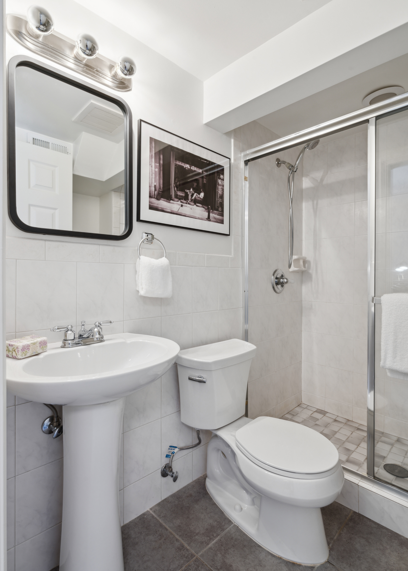 A pedestal sink, shower, toilet and mirror with chrome-dipped light bulb vanity light