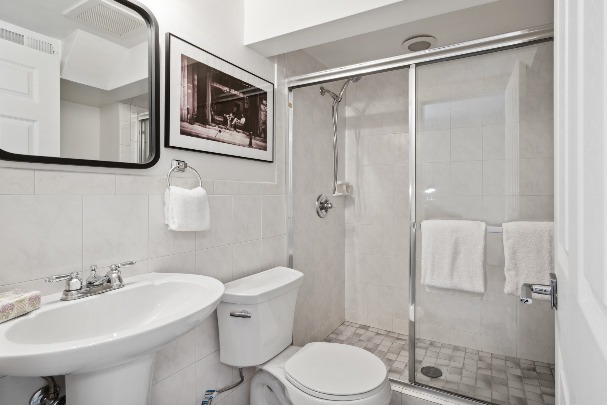 A pedestal sink, shower, toilet and mirror with chrome-dipped light bulb vanity light