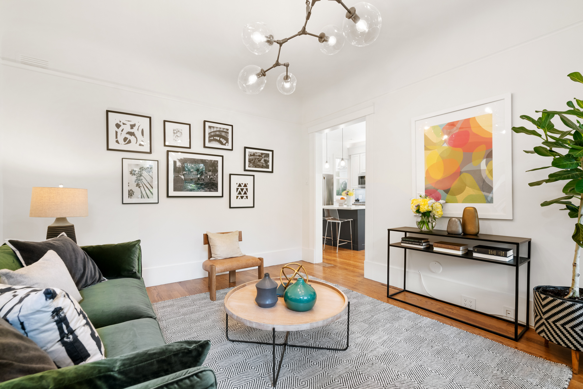 Stylish living room with gallery wall, modern decor accents, access to bright kitchen, and comfortable seating area.