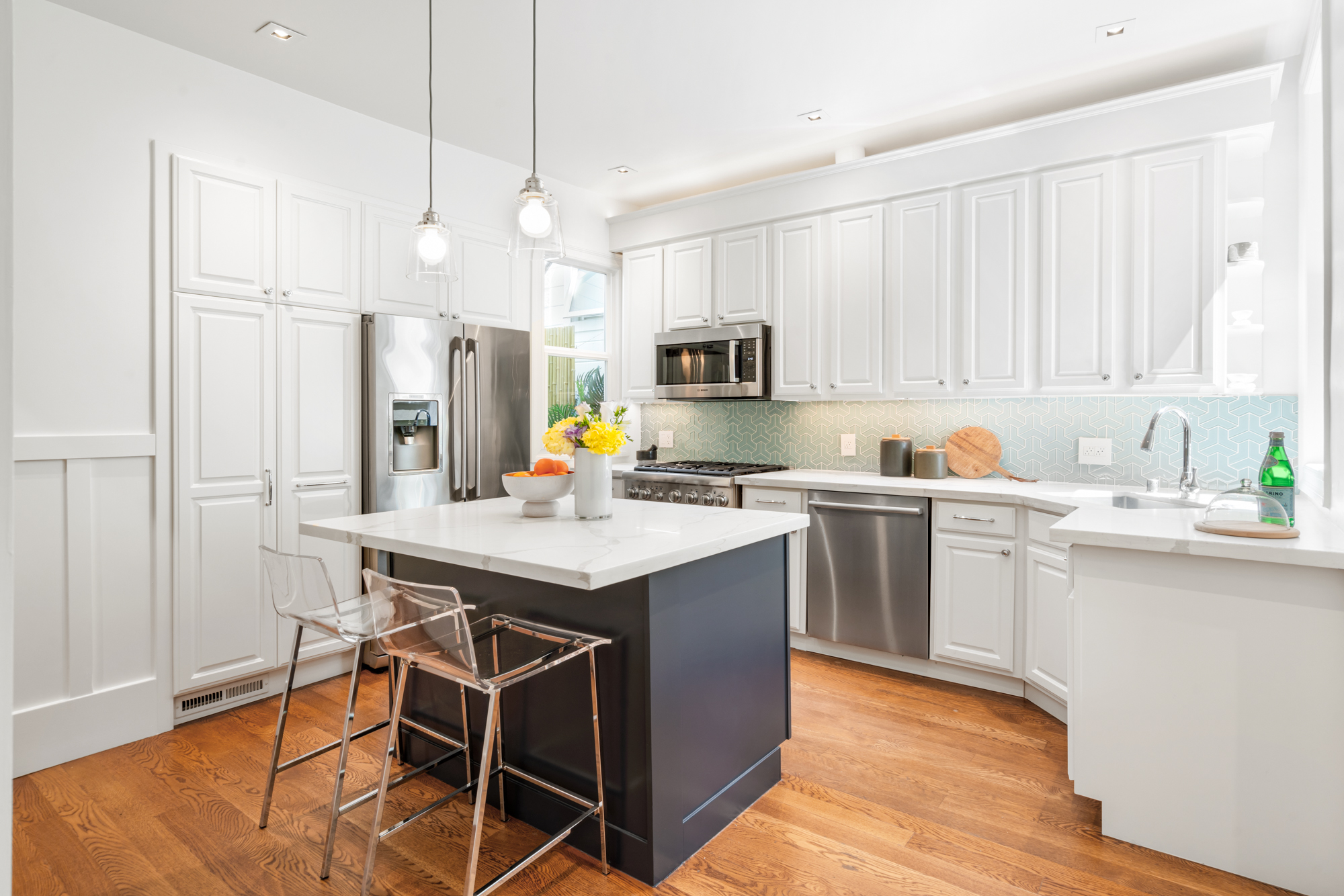 Kitchen island in rich blue tones, white quartz countertop, pendant lighting, stainless refrigerator, and ample cabinetry.