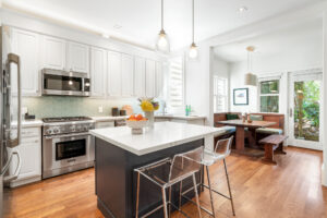 Contemporary kitchen with quartz-topped island, stainless appliances, pendant lights, designer backsplash, and adjacent dining area with garden views.”
