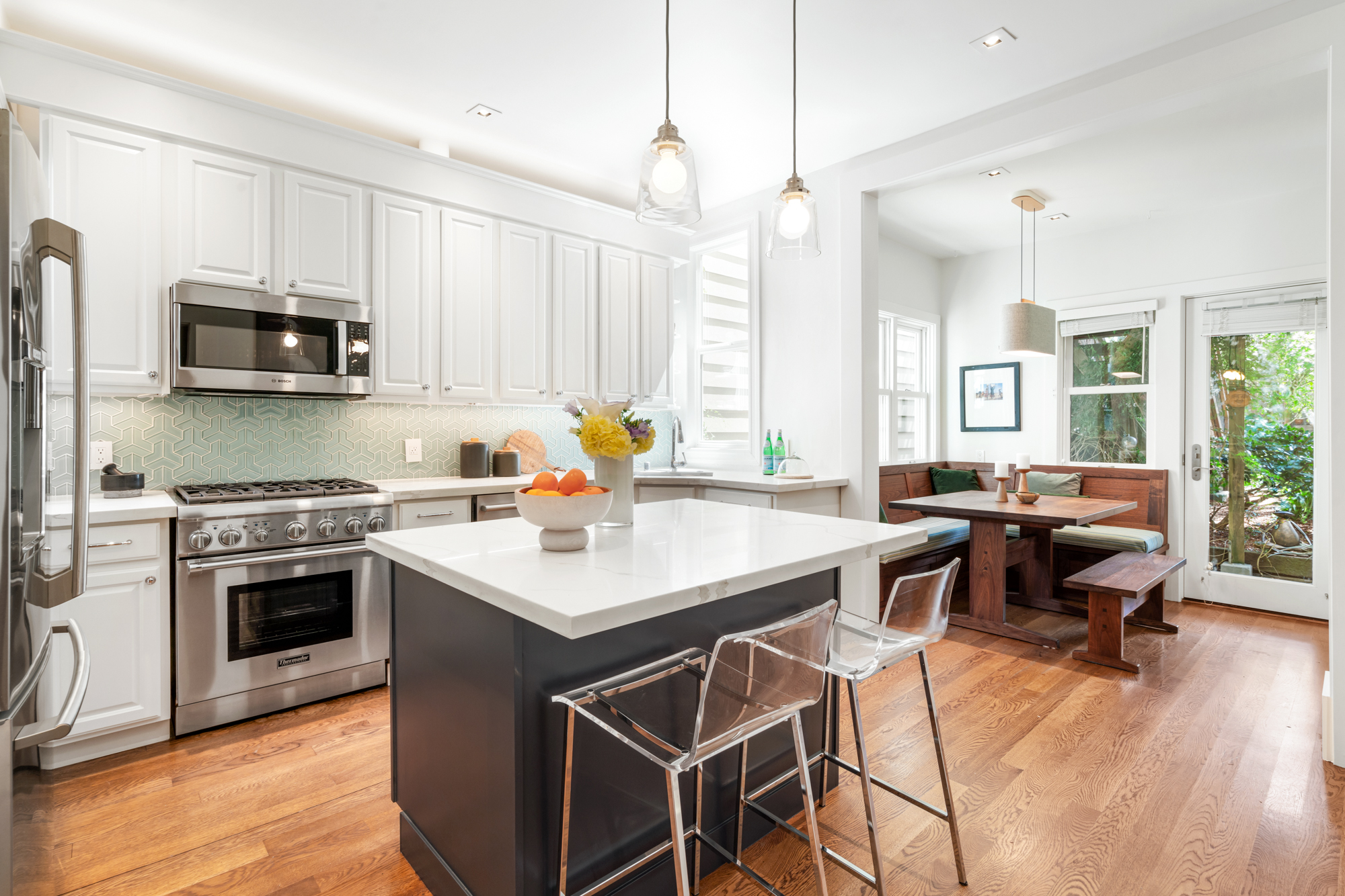 Contemporary kitchen with quartz-topped island, stainless appliances, pendant lights, designer backsplash, and adjacent dining area with garden views.”