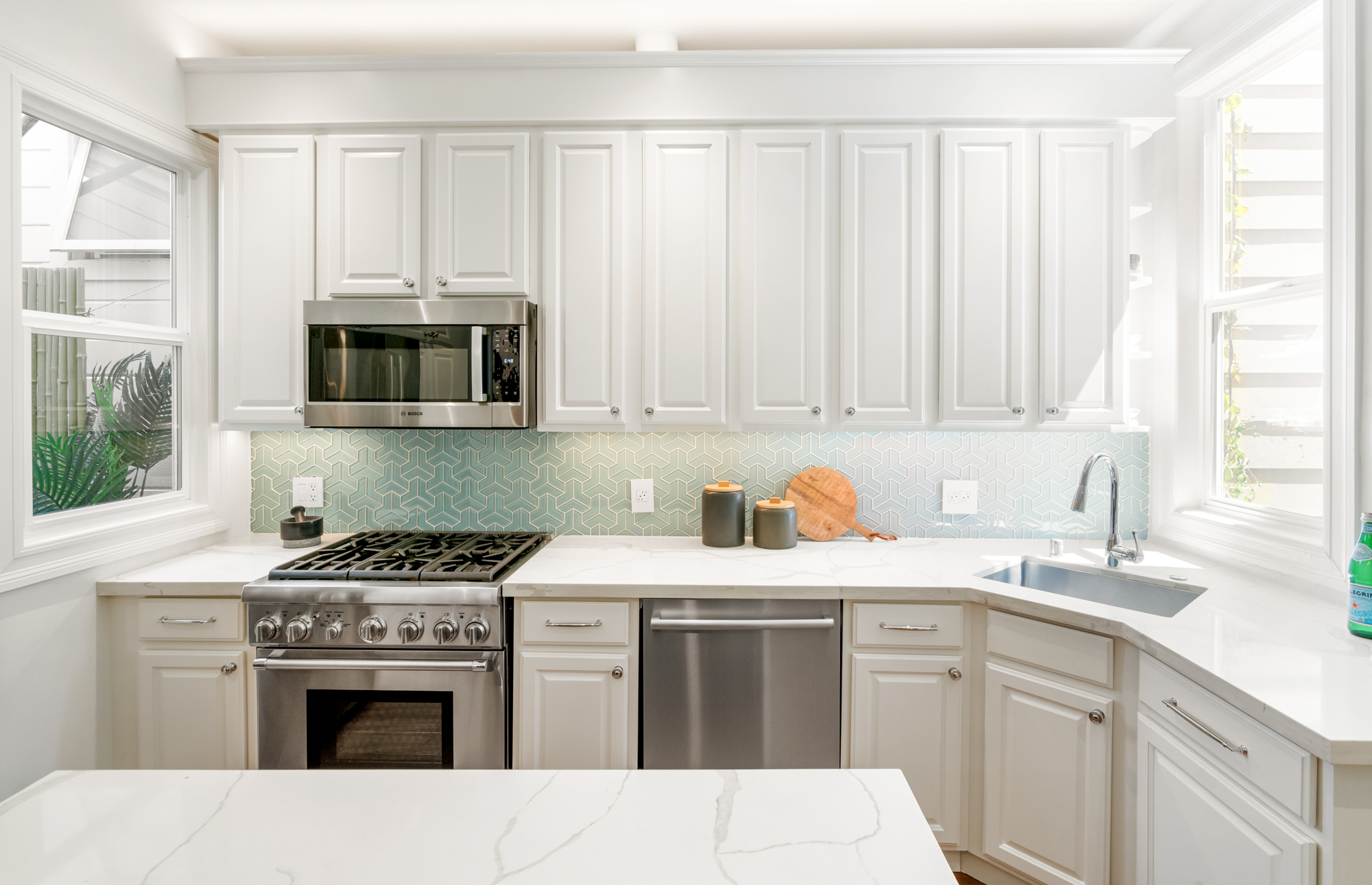 Bright kitchen with Thermador gas range, stainless appliances, quartz countertops, designer tile backsplash, and ample cabinetry