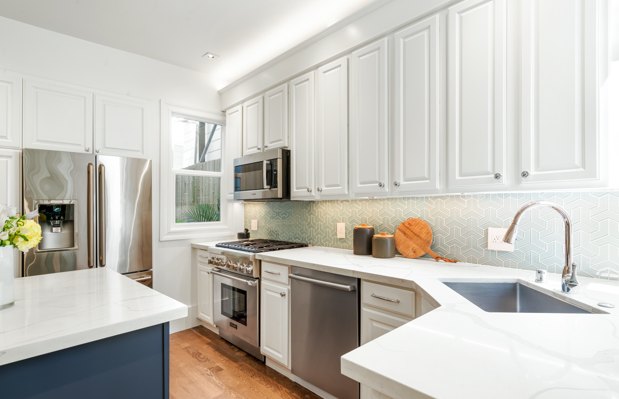 Contemporary kitchen with quartz-topped island, stainless appliances, pendant lights, designer backsplash, and adjacent dining area with garden views.”