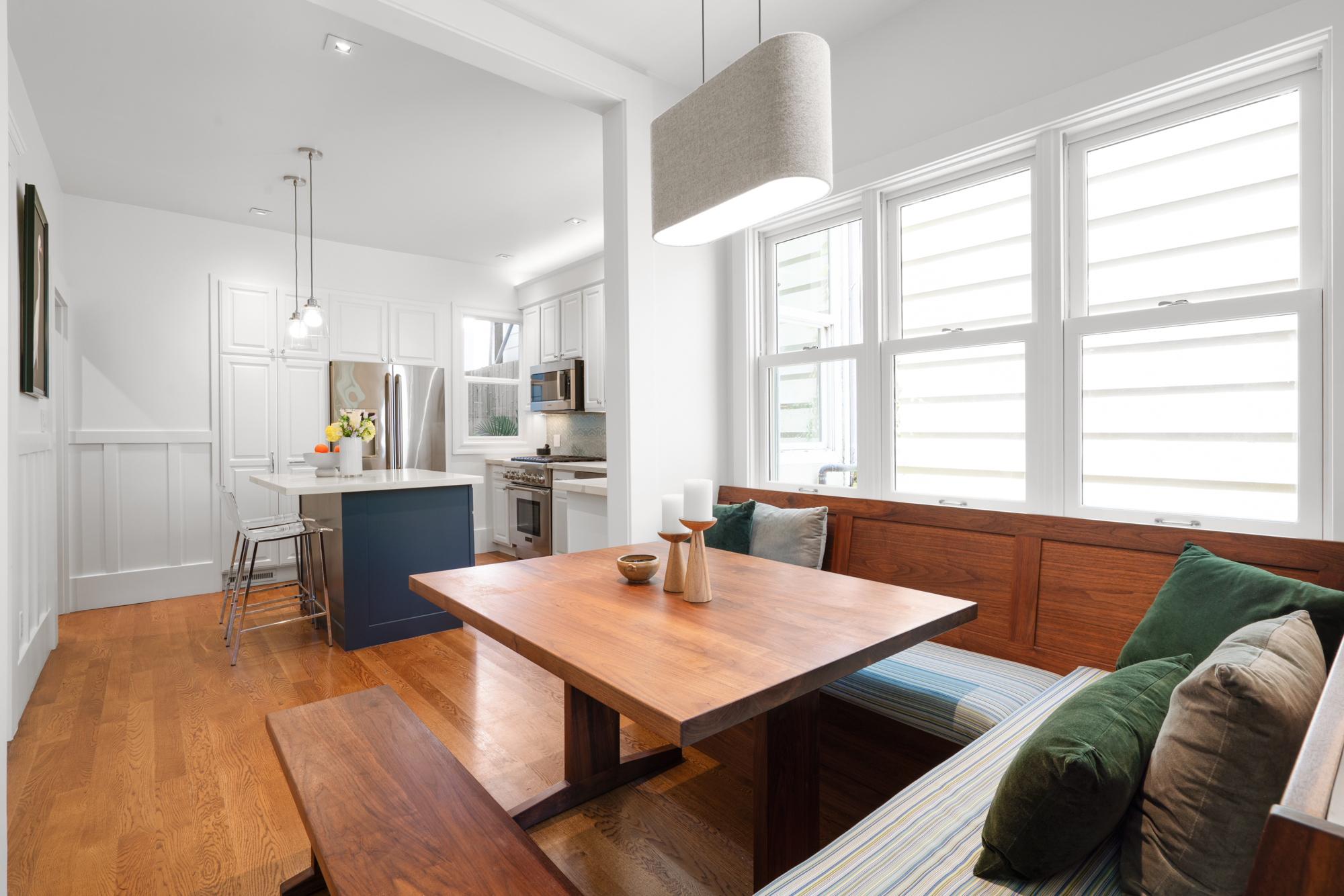 Welcoming dining nook with custom walnut table, bench seating, pendant lighting, opening directly to chic kitchen with island.