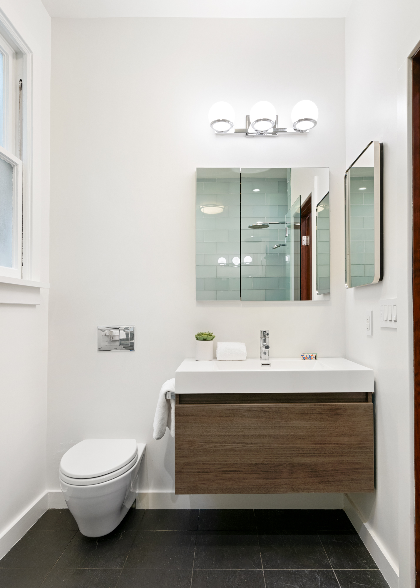 Stylish floating vanity with modern sink, wall-mounted toilet, contemporary lighting, and large mirrored cabinets