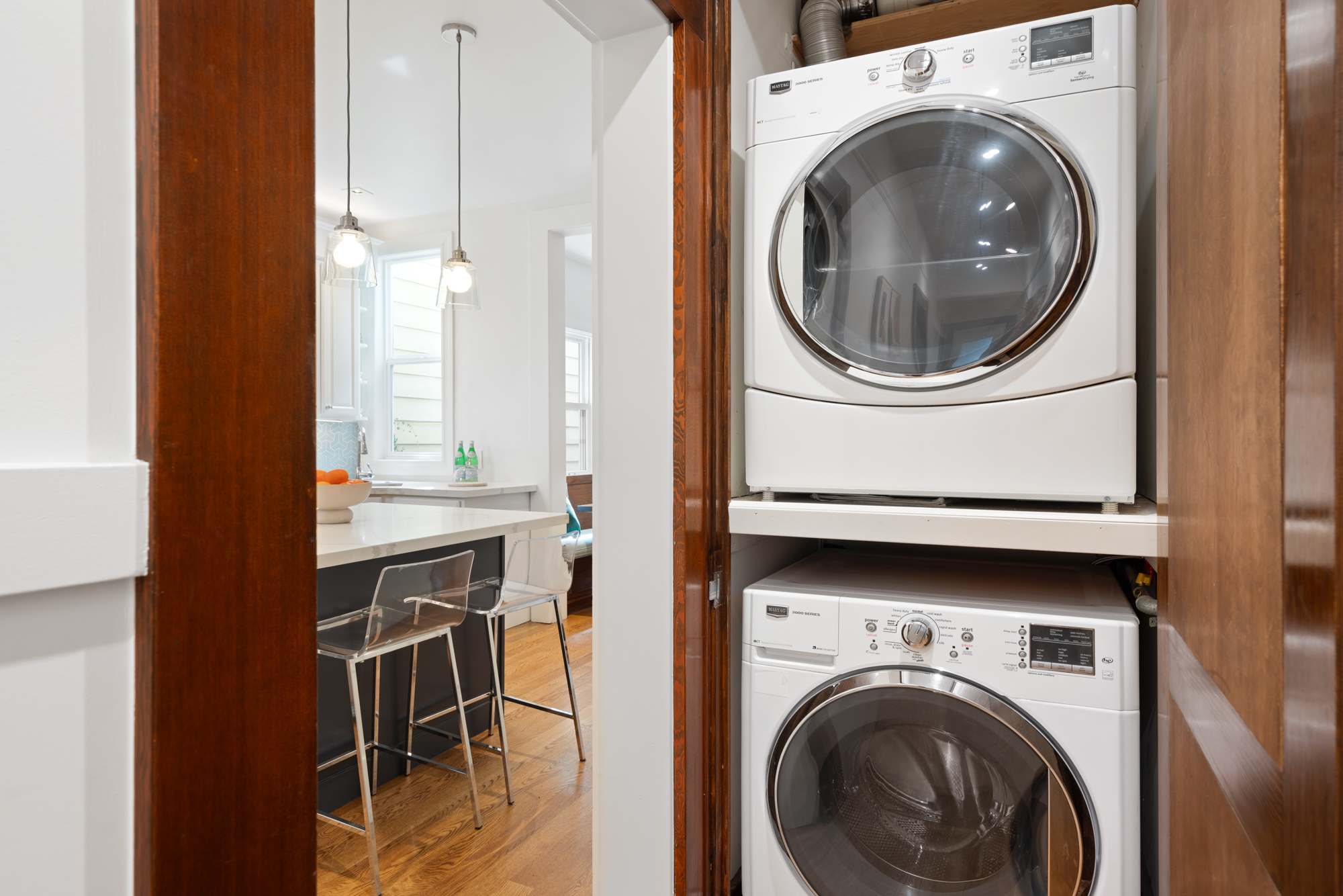 Convenient stacked laundry adjacent to sleek kitchen with island seating and designer pendant lights.