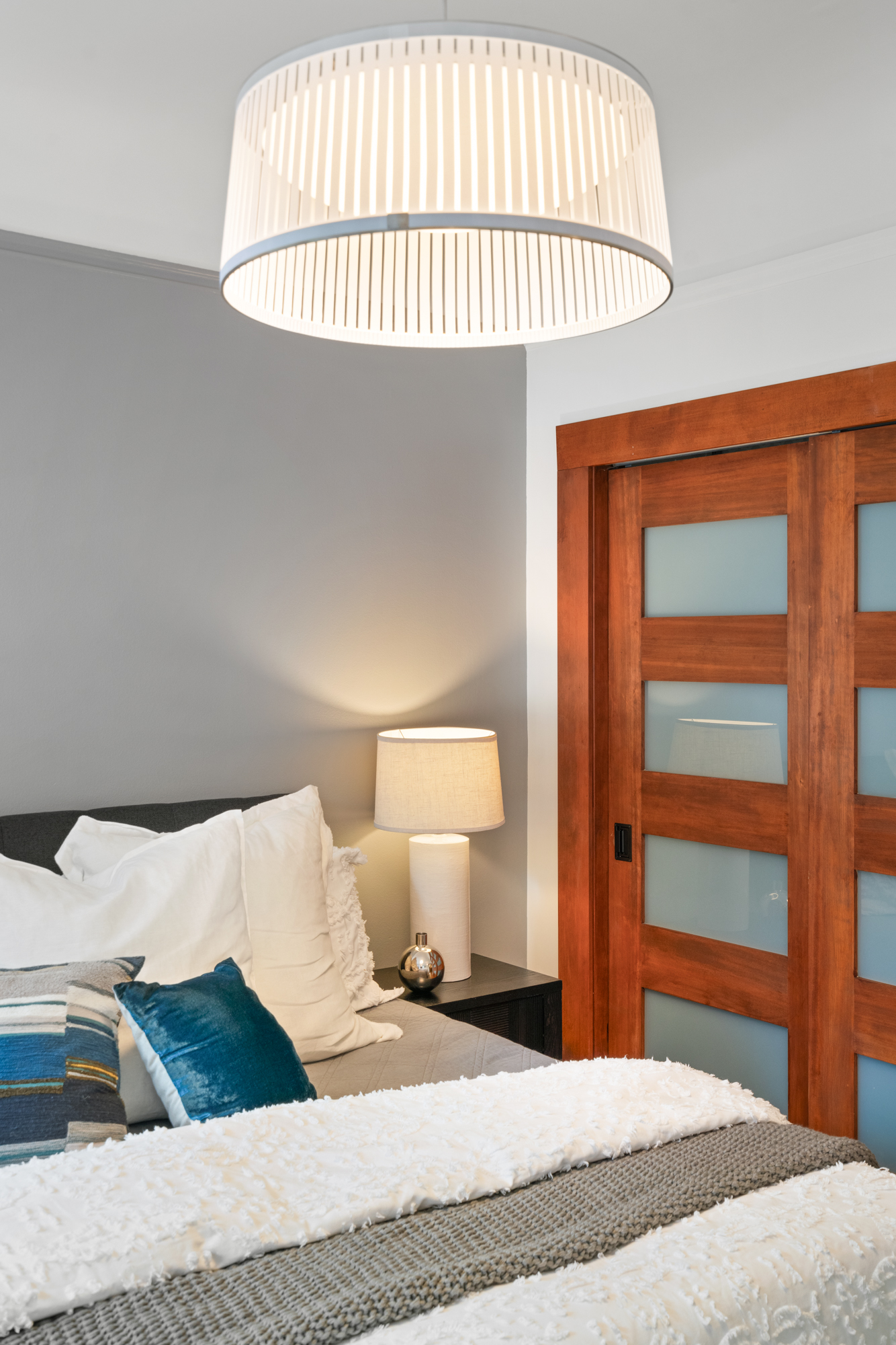Bright bedroom with hardwood floors, contemporary pendant lighting, frosted glass double doors revealing a large closet.