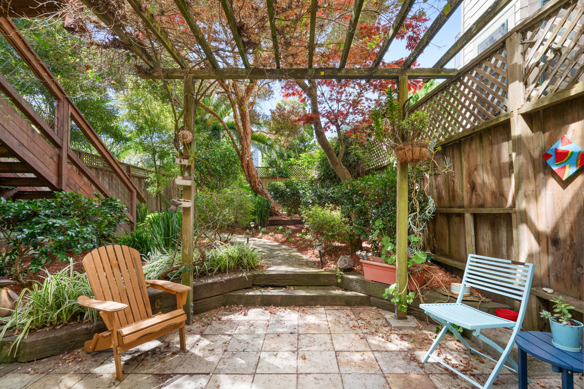 Charming garden retreat featuring pergola, mature plants, seating areas, and wooden fencing for privacy.