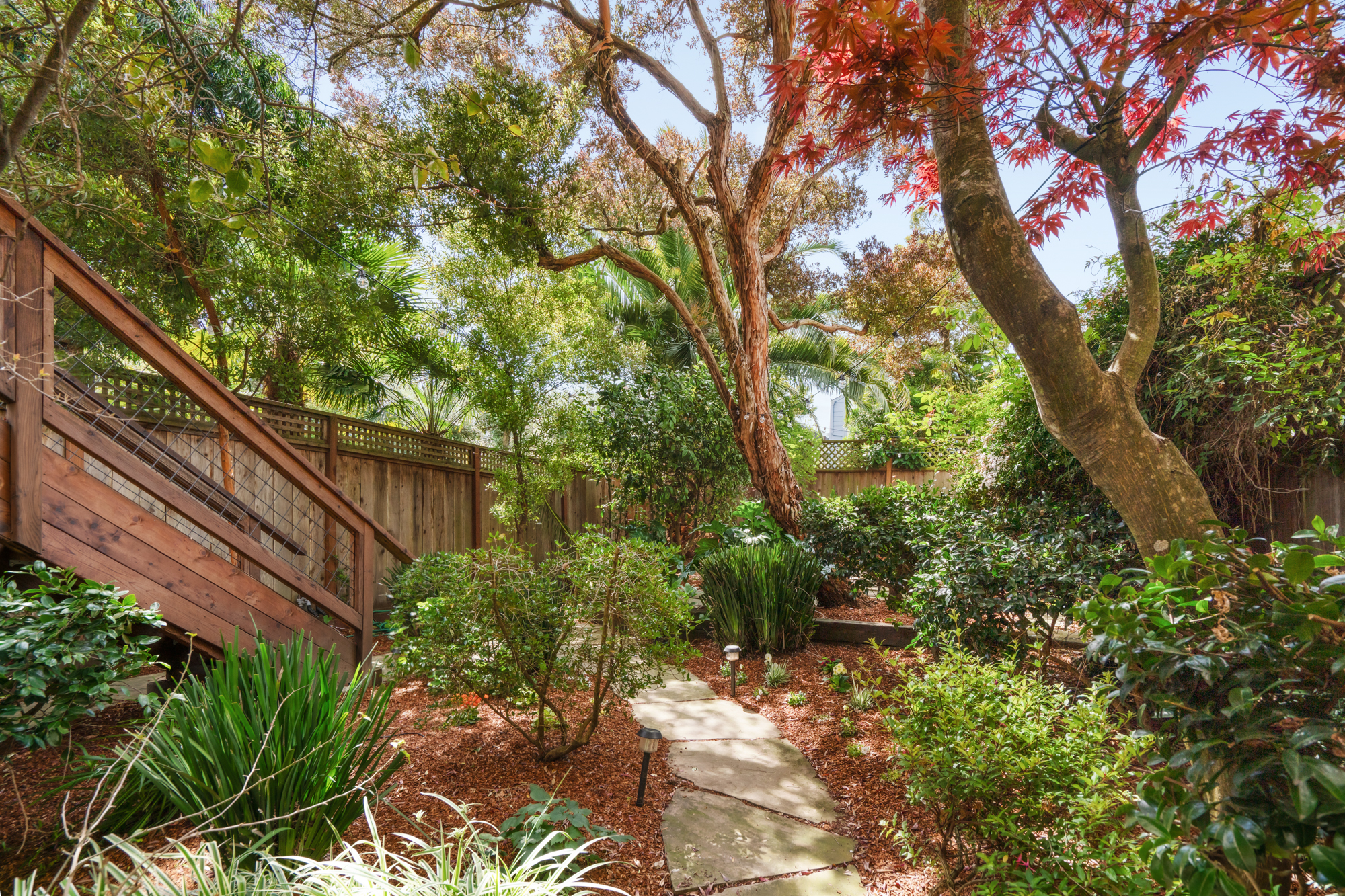 Private garden oasis with flagstone patio, lush greenery, and string lights.