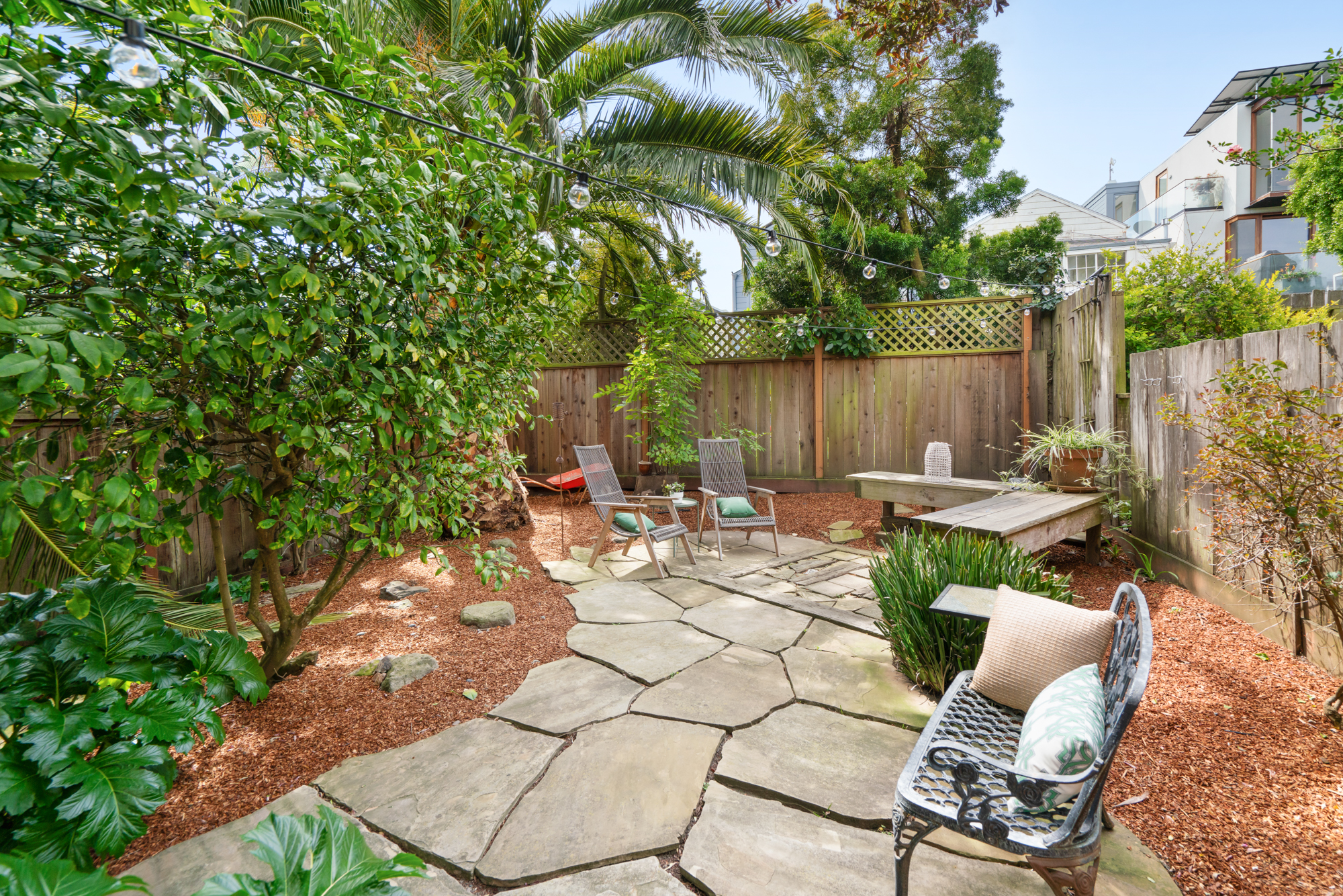 Private garden oasis with flagstone patio, lush greenery, string lights, and comfortable seating areas.