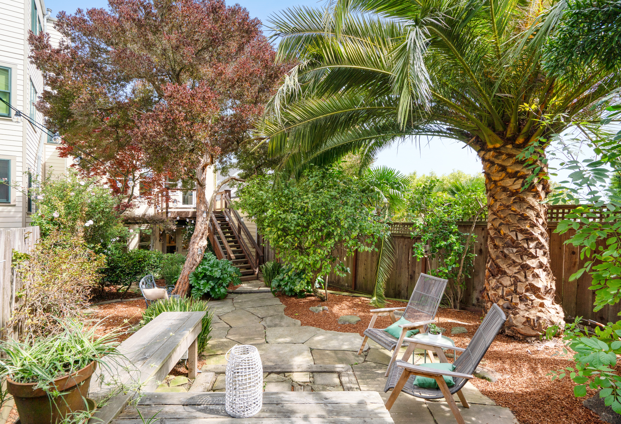Private garden oasis with flagstone patio, lush greenery, string lights, and comfortable seating areas.