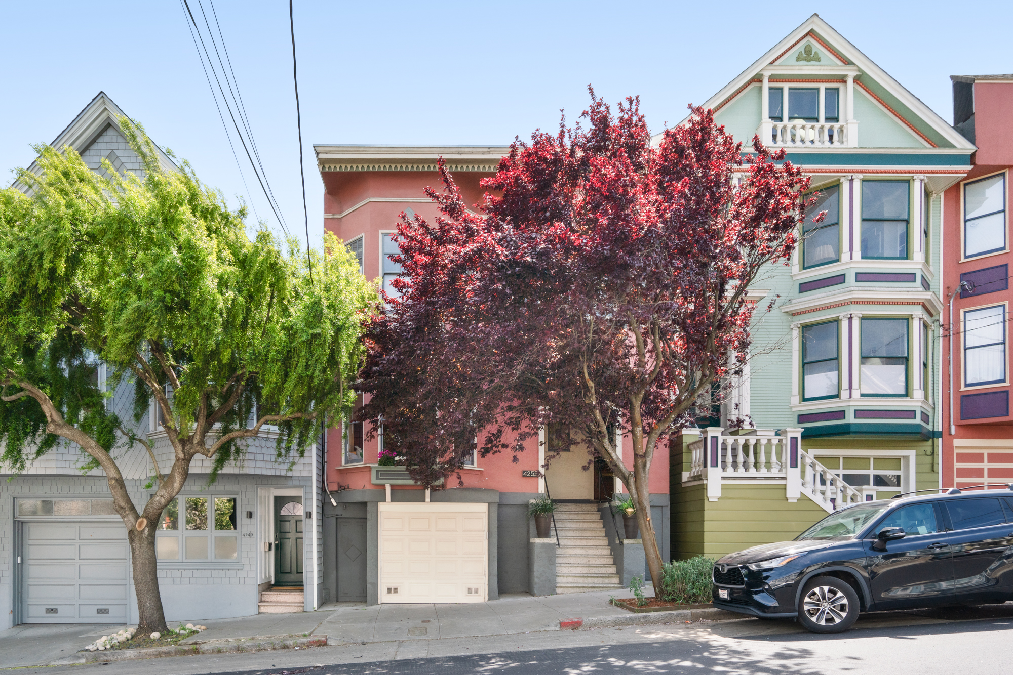 Street-level view showcasing charming pink facade of historic building, garage parking, vibrant trees, and classic San Francisco architecture.