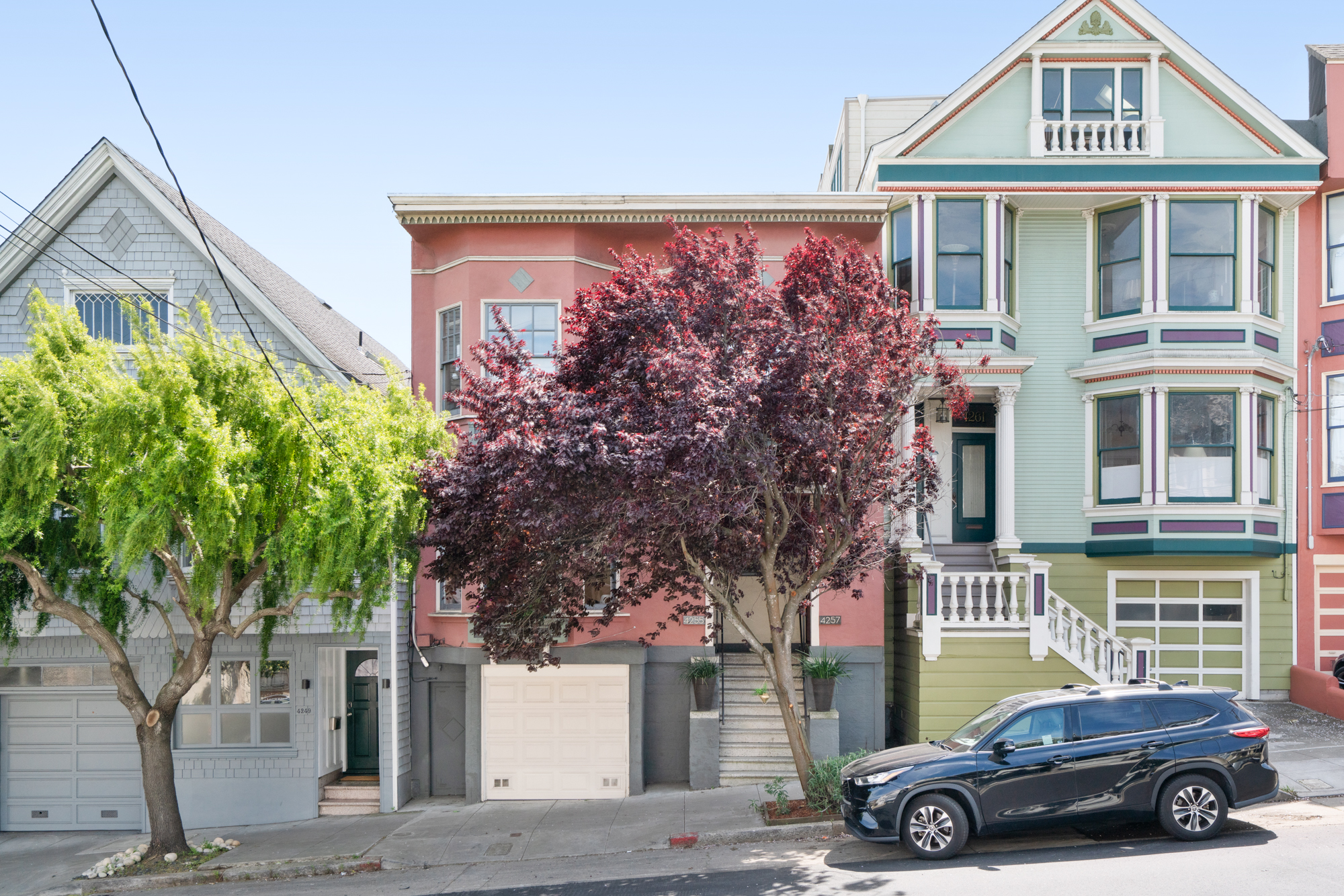 Street-level view showcasing charming pink facade of historic building, garage parking, vibrant trees, and classic San Francisco architecture.