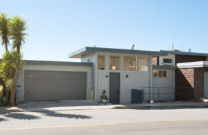 Clean mid-century façade with clerestory windows, simple rooflines, and an attached two-car garage. Gray color, Yucca tree to left.